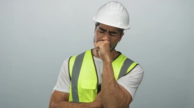 Gri stüdyoda kasklı ve neon renkli yelek giyen İspanyol bir adam yumruk yumruğa öksürüyor..