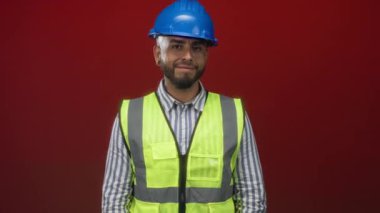 Mavi başlıklı ve yansıtıcı yelekli adam kırmızı stüdyoda kamerayı işaret ediyor..