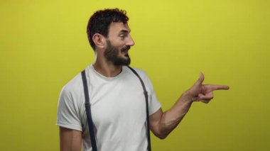 Sakallı bir adam şakacı bir tavırla sarı arka planda beyaz gömlek giyiyor telefon konuşmasını taklit etmek için elleri kullanıyor ve eğlenceli etkileşimli bir anı işaret ediyor.