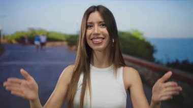 Mavi suya tepeden bakan deniz kenarında parlak bir gülümseme ile ellerini uzatan güneşli kadın; saf neşe.