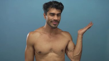 Kendine güvenen bir adam, mavi stüdyo ortamında çıplak göğsü olan avucunun içini işaret eder..