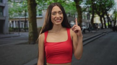 Kadın, kırmızı kırbaç giyen ve başını kaldırıp gülümseyen binaların önündeki caddeyi işaret ediyor..