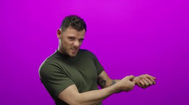 Çekici bir jest yapan genç bir adam canlı pembe arka plana karşı izole edilmiş, dışa dönük duygular ve gündelik bir tarz sergiliyor.