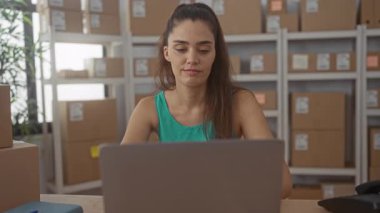 İnşaatta eli çenesinde olan kadın, paket kutularının arasında dizüstü bilgisayarı inceliyor; konsantrasyon verimliliği motivasyonu.