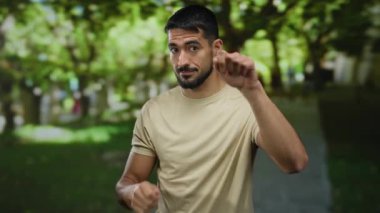 Genç adam güneşli bir parkta rastgele poz veriyor. Sıcak bir günde yemyeşil ağaçlar ve doğal güzelliklerle çevriliyken kendine güveni ve çekiciliği yayıyor..