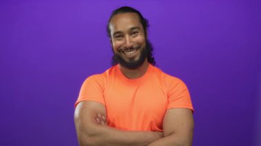 Stüdyoda kolları bağlı gülümseyen bir adam mor arka planda; güven dostça pozitif enerji.
