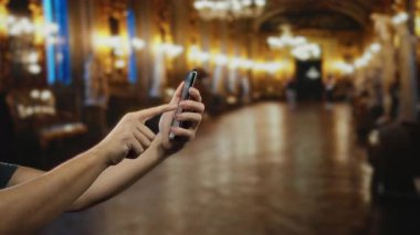 Süslü müze odasında akıllı telefon kullanan bir adam zarif tarihsel ortamda teknolojiyle etkileşim içinde olan ellerini sergiliyor..