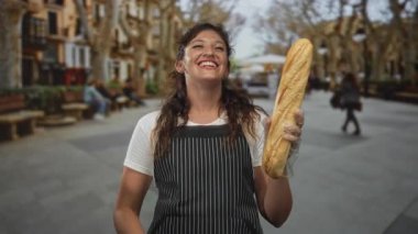 Banklar ve ağaçlarla dolu kalabalık bir sokak parkında elinde baget tutan ve önlük ve plastik eldiven giyen bir kadın..