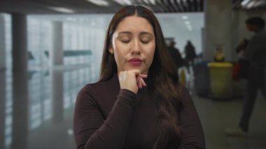 Geniş, modern havaalanı terminalinde elleri çenesinde, cam pencereleri ve gözleri kapalı duran kadın, tefekkür.