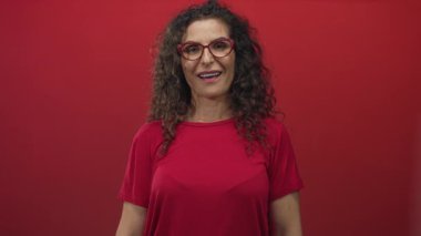 Kırmızı gözlüklü kadın stüdyoda el sıkışmak için elini uzatıyor; dostça selamlaşma bağlantısı.