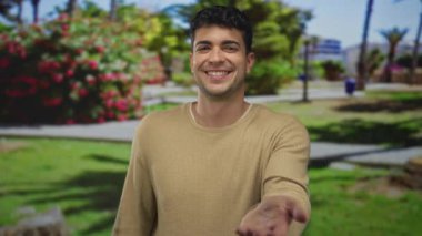 Bir adam parkın karşısından elini uzatıyor, İspanyol genç erkek avucu açık havada gülümsüyor..
