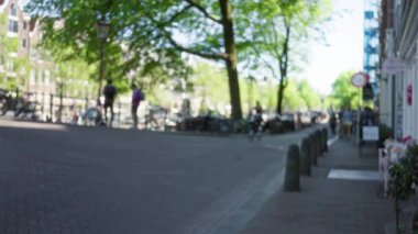 Hollanda 'daki ağaçların ve kanalların canlı zeminine odakları kesilmiş insanlar ve bisikletlerin bulanık görüntüsü.