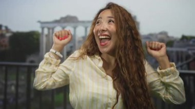 Ağzı açık bir kadın gülüyor ve yumruklarını Roma harabelerine kaldırıyor. Kırık kolonlara ve taş kemer yoluna bakan teras inşa ediyor..