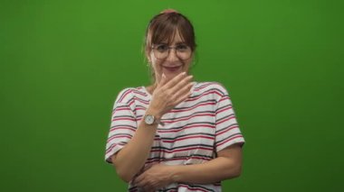 Yeşil stüdyoda ağzı kapalı ve karnını tutan, çizgili gömlek ve gözlük takan bir kadın, eğlenceli bir eğlence..