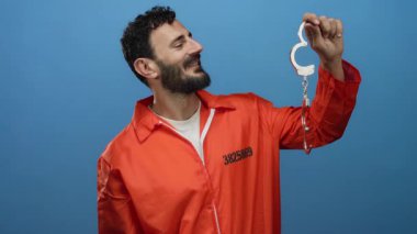 Turuncu hapishane tulumlu, mavi arka planda kelepçeli İspanyol sakallı adam tutukluluk temasını betimliyor..