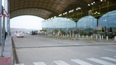 Bokeh efektli yoğun bir seyahat ortamında 1 numaralı havaalanı terminalinin bulanık dış görünümü odaklanmış yapıyı ve araçları gösteriyor ve arka planda insanları bulanıklaştırıyor.