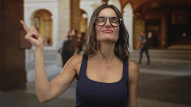 Gözlüklü genç İspanyol kadın güneş ışığı altında eski kasaba sokaklarındaki kemeri işaret ediyor..