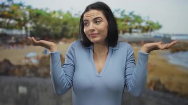 Mavi gömlekli kadın plajda kafa karışıklığı yaşıyor. Deniz manzarasının bulanık arka planı var..