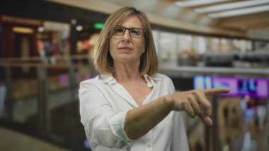 Orta yaşlı, gözlüklü sarışın kadın parmak işaretleri bina koridorunda. Kararlılık..