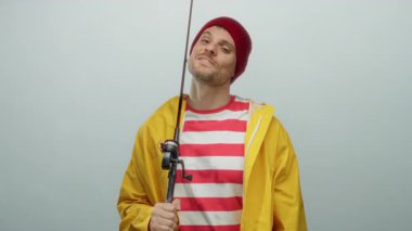 Elinde olta tutan genç bir adam, sarı yağmurluk ve kırmızı bir bere takıyor, beyaz bir arka plana güvenle gülümsüyor, yakışıklı, neşeli ve sıradan bir havayı somutlaştırıyor..