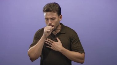 Mor bir stüdyoda, bir eli göğsüne sıkışmış, yumruğuna öksüren genç İspanyol bir adam. Hastalık endişesi..