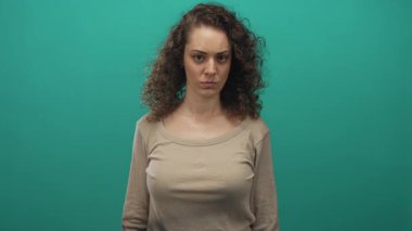 Genç bir kadın açık ağızla bağırıyor, alnı çatık, bej rengi bluz ve kıvırcık saçlar giyiyor. Öfke..