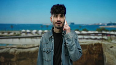 Manzaralı deniz kıyısında, arka planda okyanus manzaralı akıllı telefondan konuşan bir adam günlük şehir yaşam tarzını sergiliyor..