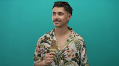 Dondurmalı genç adam yeşil arka planda, çiçekli gömlek giyiyor, yana bakıyor, rahat bir turist havasını somutlaştırıyor..