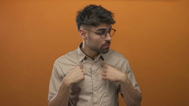 Stüdyoda parlak turuncu arka planı olan bir gömlek yakasını gösteren bir adam parmağı, meraklı bir bakışla çerçevelenen gözlükler; şüphe..