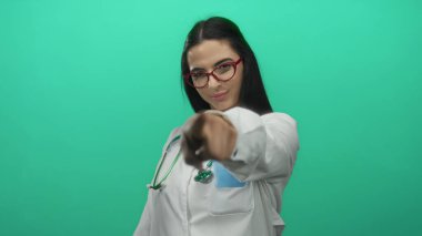 Üniformalı İspanyol kadın doktor boynunda bir steteskopla yeşil arka plan duvarını işaret ediyor..