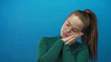 Stüdyoda mavi duvara el ele tutuşan gözlüklü, yeşil kazaklı genç beyaz kadın, uykusuzluk..