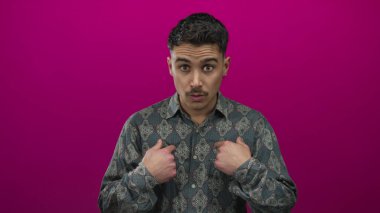 Genç İspanyol bir adam şaşkın ve kendini işaret ediyor canlı pembe bir arka plan, ifade ve duygu vurguluyor.