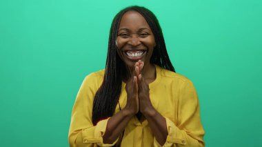 Canlı yeşil bir arkaplan önünde mutlu bir şekilde gülümseyen kadın, sarı bir gömlek giyiyor, pozitiflik ve sıcaklık yayıyor, sade bir arkaplanda izole edilmiş.