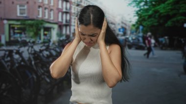 Beyaz bluzlu genç kadın şehir caddesinde el ele tutuşuyor ve yüzünü buruşturuyor. Duyusal aşırı stres..