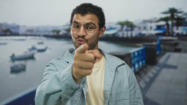 Mavi ceketli ve gözlüklü bir adam iskele tarafındaki güvertede kamerayı işaret ediyor; özgüven daveti motivasyon bağlantısı ilhamı teşvik etme hevesini güçlendiriyor.