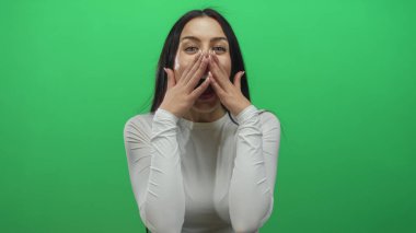 Beyaz bluzlu İspanyol kadın yeşil arka plan duvarından duyduğu neşeyi ifade ediyor. Elleri yüzlerinde, olumlu duygular gösteriyor..