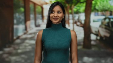 Kapalı gözlü genç bir kadın arka planda ağaçlar ve arabalarla şehir sokağının tadını çıkarıyor. Sıcak güneş ışığı altında huzurlu bir atmosfer yaratıyor.