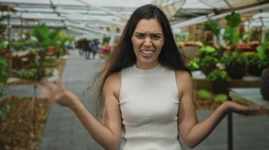 Çiçek pazarı binasında, saksı bitkileri ve çiçeklerle çevrili bir kadın omuz silkiyor. Hayal kırıklığı..