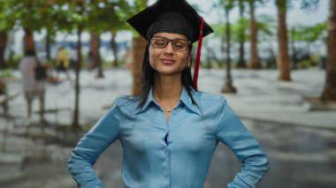 Mezuniyet şapkalı kadın, açık havada kendinden emin bir şekilde duruyor, canlı bir şehir ortamında başarı ve başarıyı somutlaştırıyor..