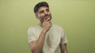 Stüdyoda elleri çenesinde açık bej gömlek giyen bir adam soluk açık yeşil ayara karşı fikirler düşünüyor; yansıma.