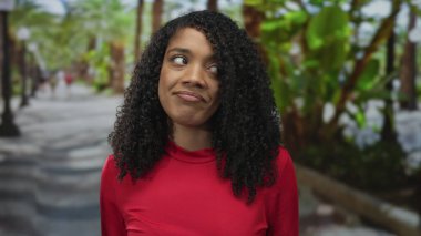 Kadın geniş, güneşli yeşil park yolunda omuzlarını silkiyor palmiye ağaçlarıyla kaplı; belirsizlik kabulü.