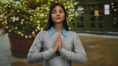 Gecenin bir yarısı şehir caddesinde, şenlikli ışıkların önünde huzur içinde meditasyon yapan bir kadın, sakin ve huzurlu bir ifade sergiliyor..