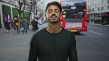 Bulanık kalabalıklar ve yüksek binalar arasında kalabalık şehir caddesinde kırmızı otobüsü işaret eden adam, kendine güvenen farkındalık.