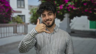 Sakallı genç adam, açık şehir sokağında çiçeklerle telefonla konuşuyor. Aydınlık bir günde iletişim ve mutluluğu ifade ediyor..