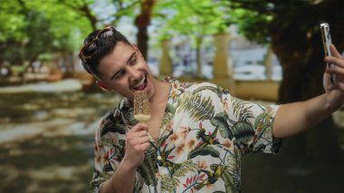 Genç adam yemyeşil bir parkta canlı bitki örtüsüyle selfie çekerken dondurmanın tadını çıkarıyor. Açık hava eğlencesi ve maceranın özünü yakalıyor..