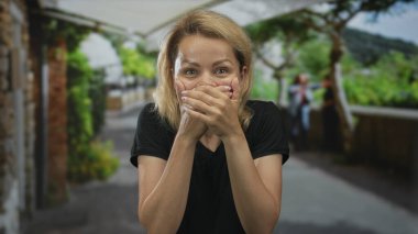 Sarışın kadın, iki eli ağaçlarla ve taş duvarlarla kaplı caddede ağzı kapatıyor. Sürpriz!.