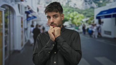 Koyu renk tişörtlü genç İspanyol adam, geride bulanık yayalar bırakarak çenesine yakın yumruklarını sıkıyor..