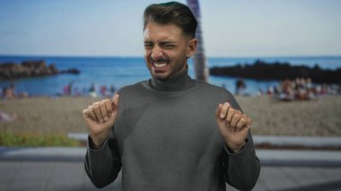 Güneşli kumlu sahilde işaret parmaklarını yukarı kaldırarak sırıtan adam, neşeli bir heyecan..