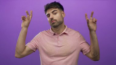 Pembe polo tişörtlü İspanyol bir adam mor stüdyoda iki eliyle tırnak işareti yapıyor. İğneleme..