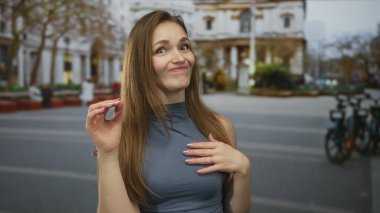 Uzun kahverengi saçlı bir kadın, sağ eliyle iyi bir işaret veriyor ve kalabalık sokak sahnesinde sol eliyle baş parmak işareti yapıyor. Onaylandı..